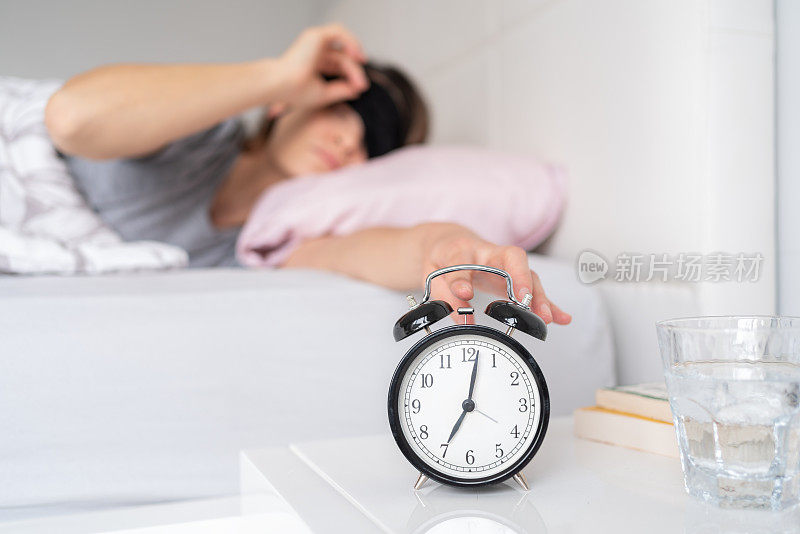 Young Woman Reaching For Her Alarm Clock After Waking Up İn Bed At Home